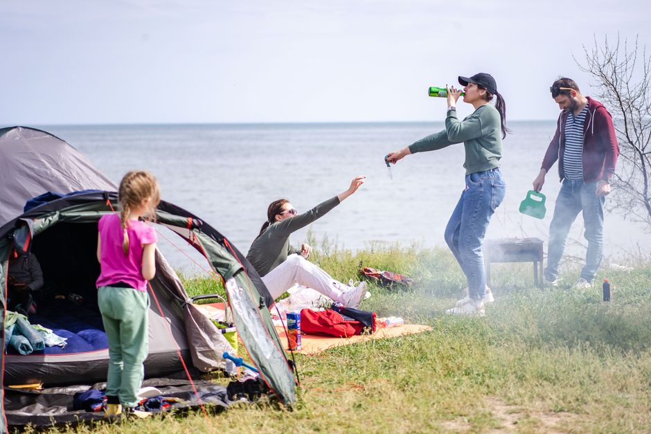 A family relaxes by the lakeside enjoying a camping picnic on a sunny day.