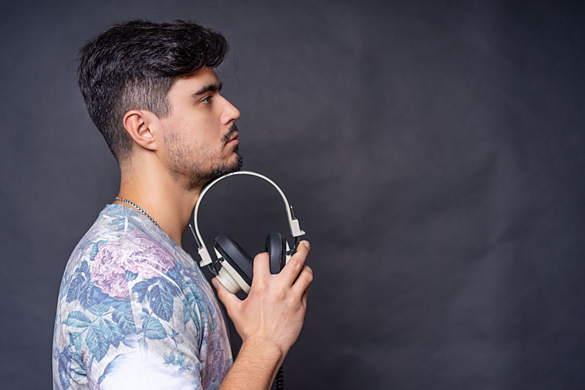 Side view portrait of a man holding headphones in a studio setting against a dark background.