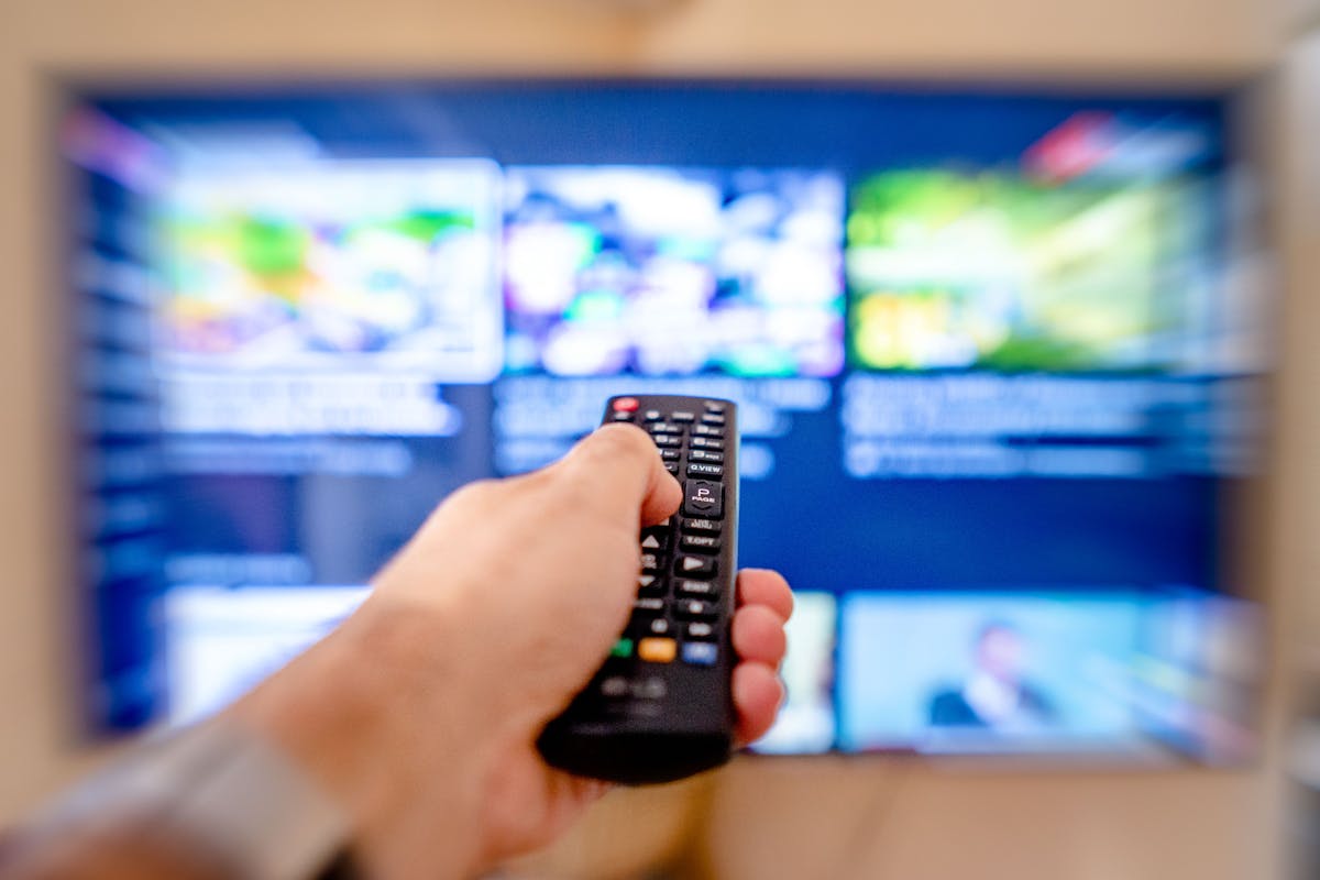 Mano che tiene un telecomando puntato verso uno schermo TV sfocato