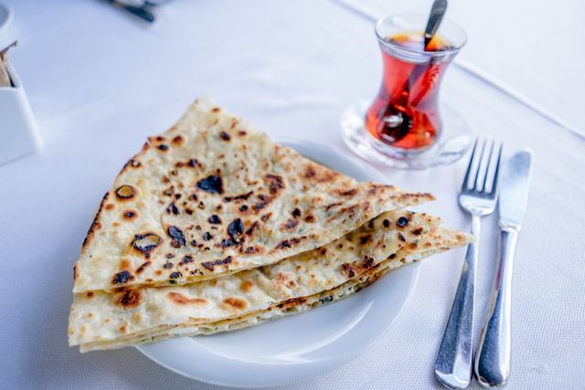 Close-up of Turkish flatbread with cutlery and tea, captured from above.