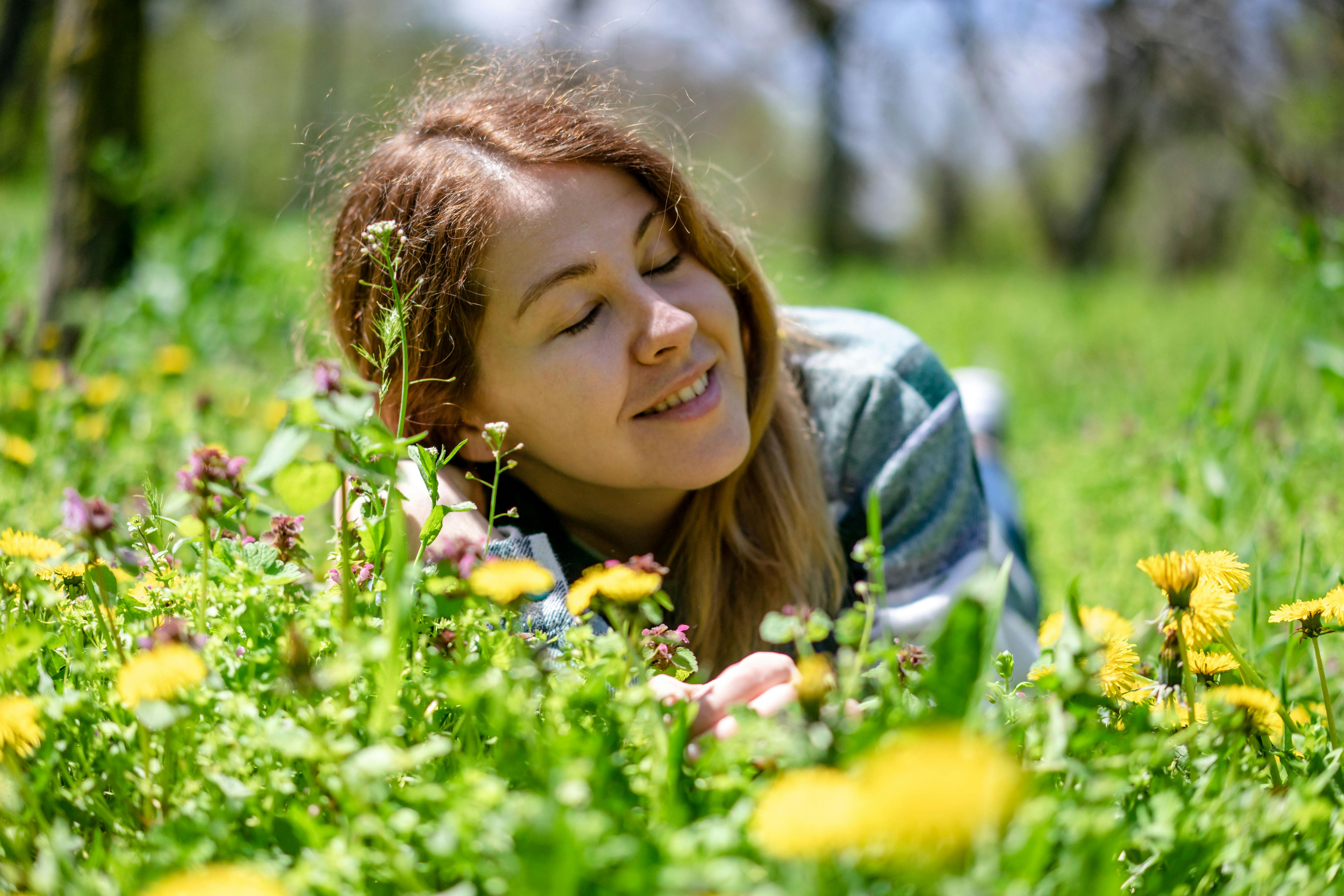 Woman enjoying a sunny day lying among blooming spring flowers in a green meadow.