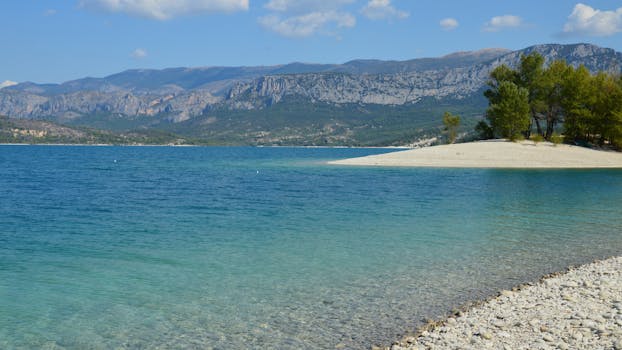 A serene turquoise lake with mountain backdrop under a clear blue sky.
