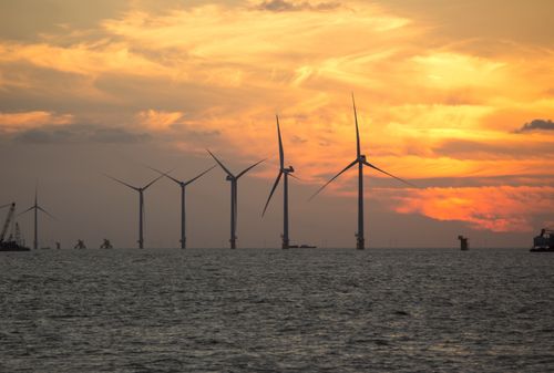Free A serene view of wind turbines silhouetted against a vibrant sunset over the sea, showcasing renewable energy. Stock Photo