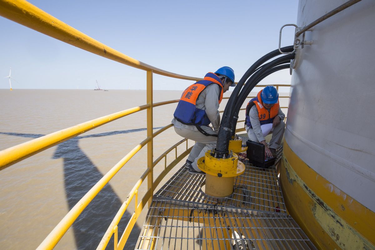Technicians in safety gear performing maintenance on an offshore wind turbine. Illustrative editorial photograph.