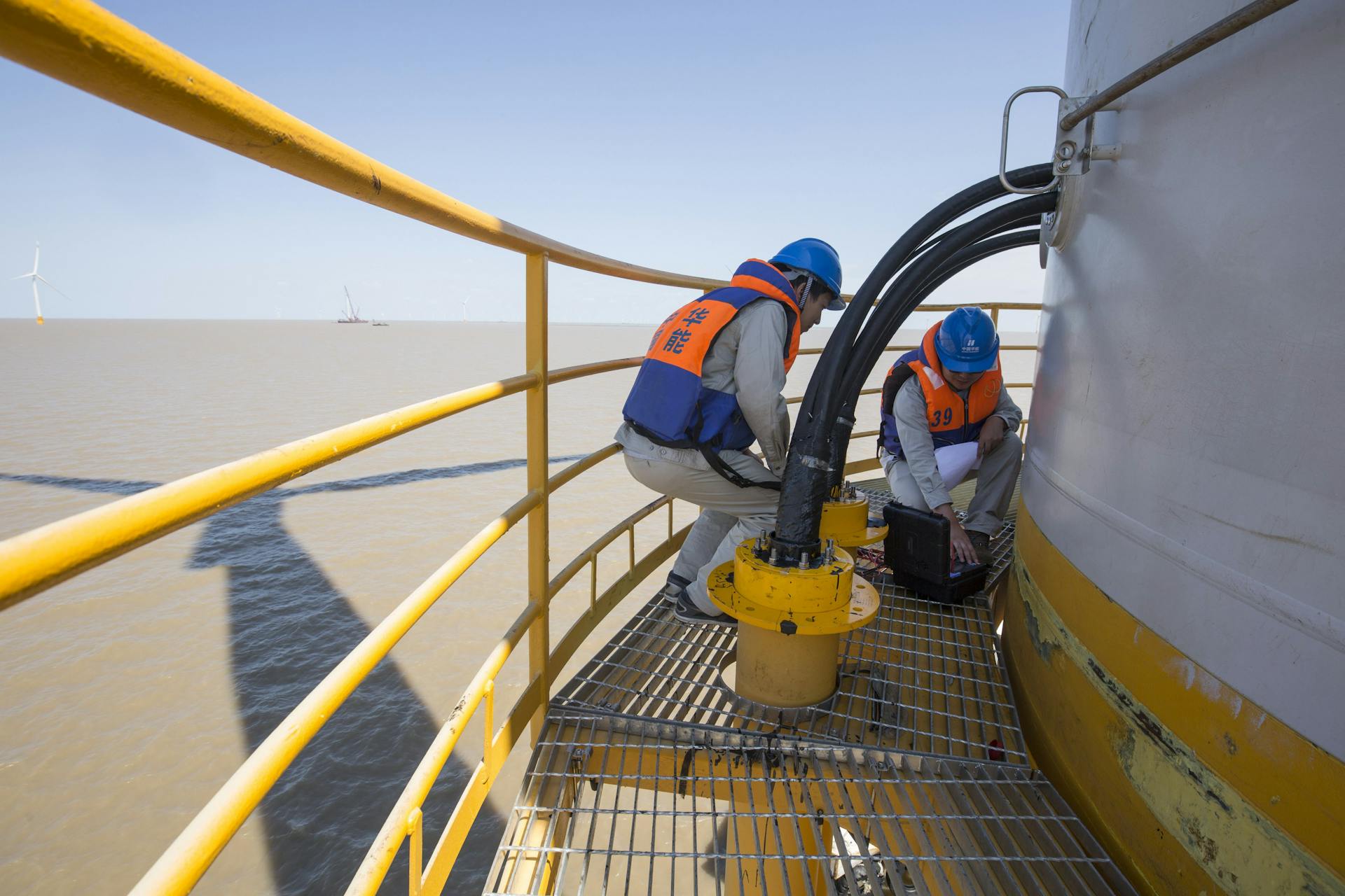 Technicians in safety gear performing maintenance on an offshore wind turbine.