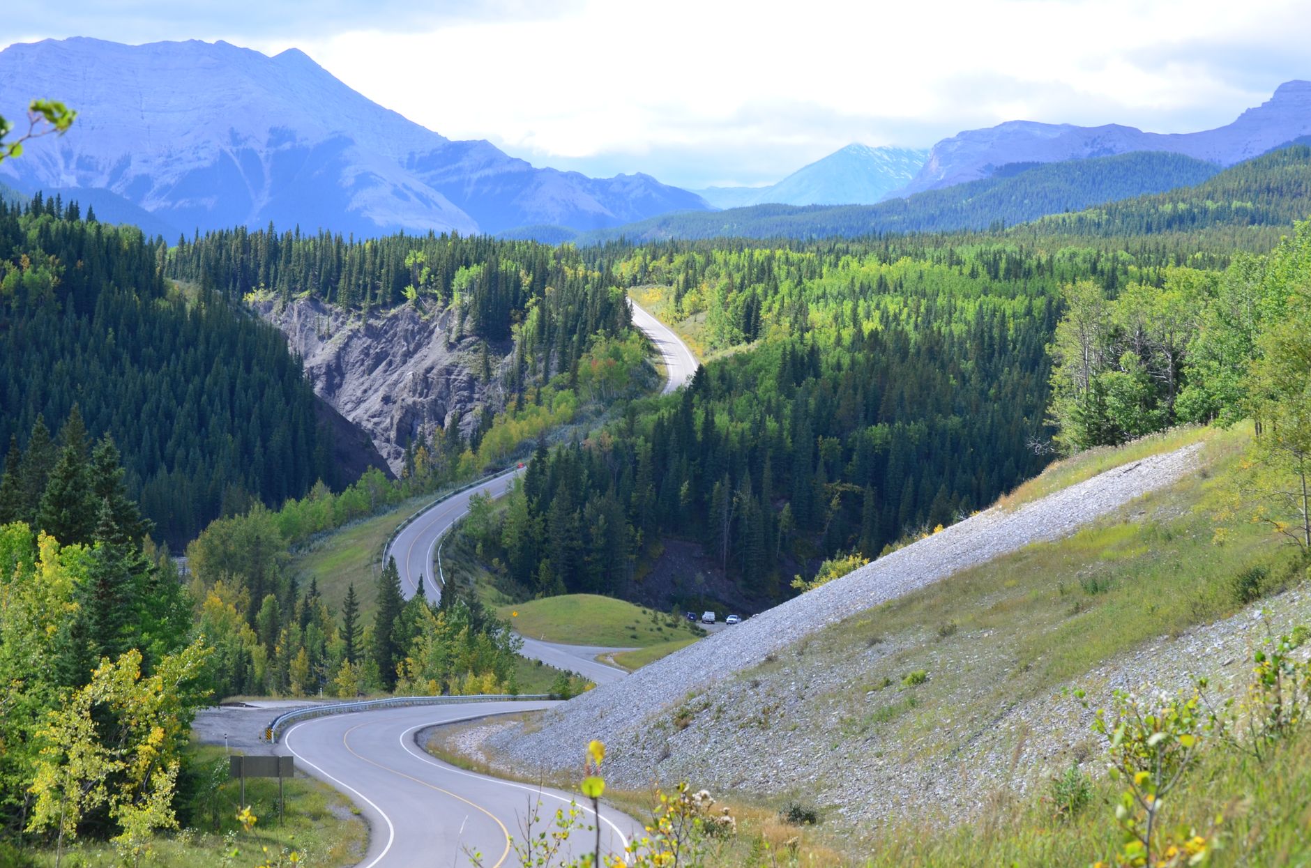 A breathtaking view of a winding road through a lush forest and majestic mountains.