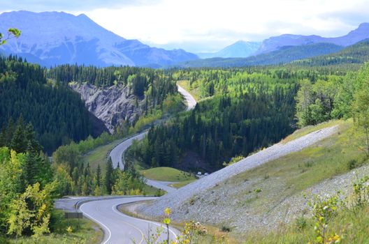 A breathtaking view of a winding road through a lush forest and majestic mountains.
