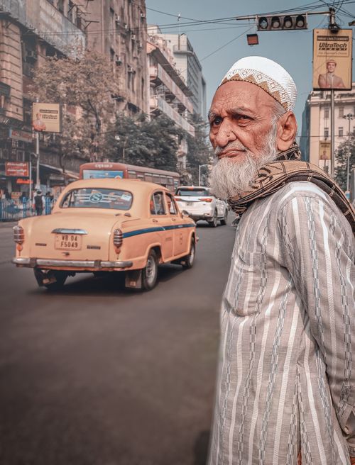 Free An elderly man with a beard stands by a bustling street in Kolkata, showcasing urban life and culture. Stock Photo
