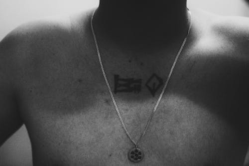 A Grayscale of a Tattooed Man Wearing a Necklace