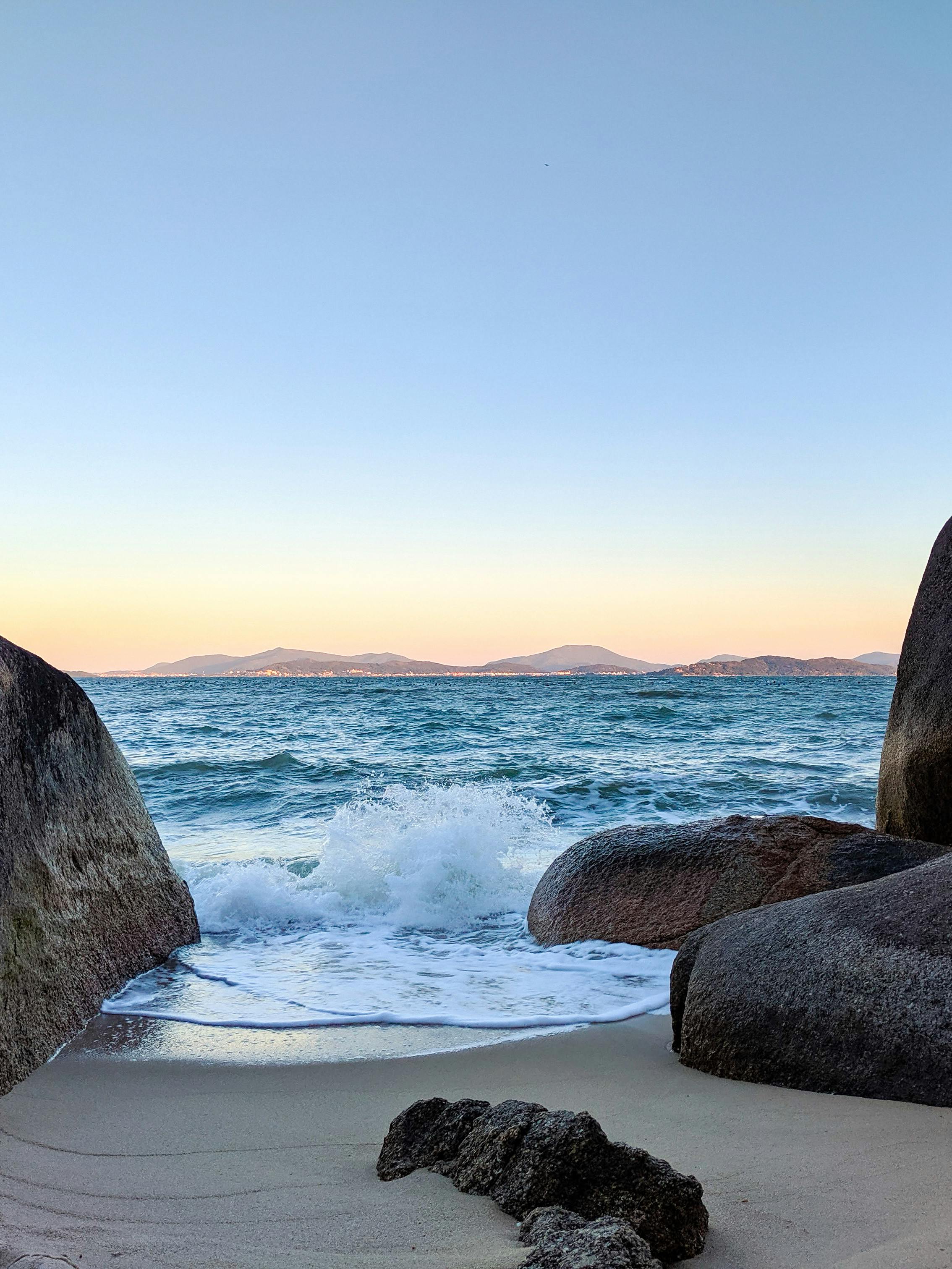Scenic ocean view with rocks and crashing waves at Governador Celso Ramos during sunset.