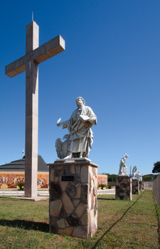 Statues of apostles with a large cross in Brasilia under a clear blue sky.