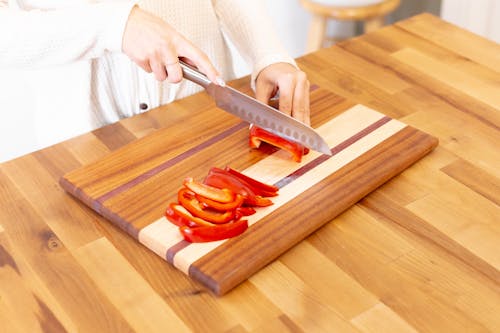 A Person Slicing a Red Bell Pepper on a Wooden Chopping Board
