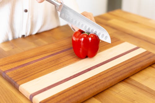 A Person Slicing Red Tomato on Brown Wooden Chopping Board