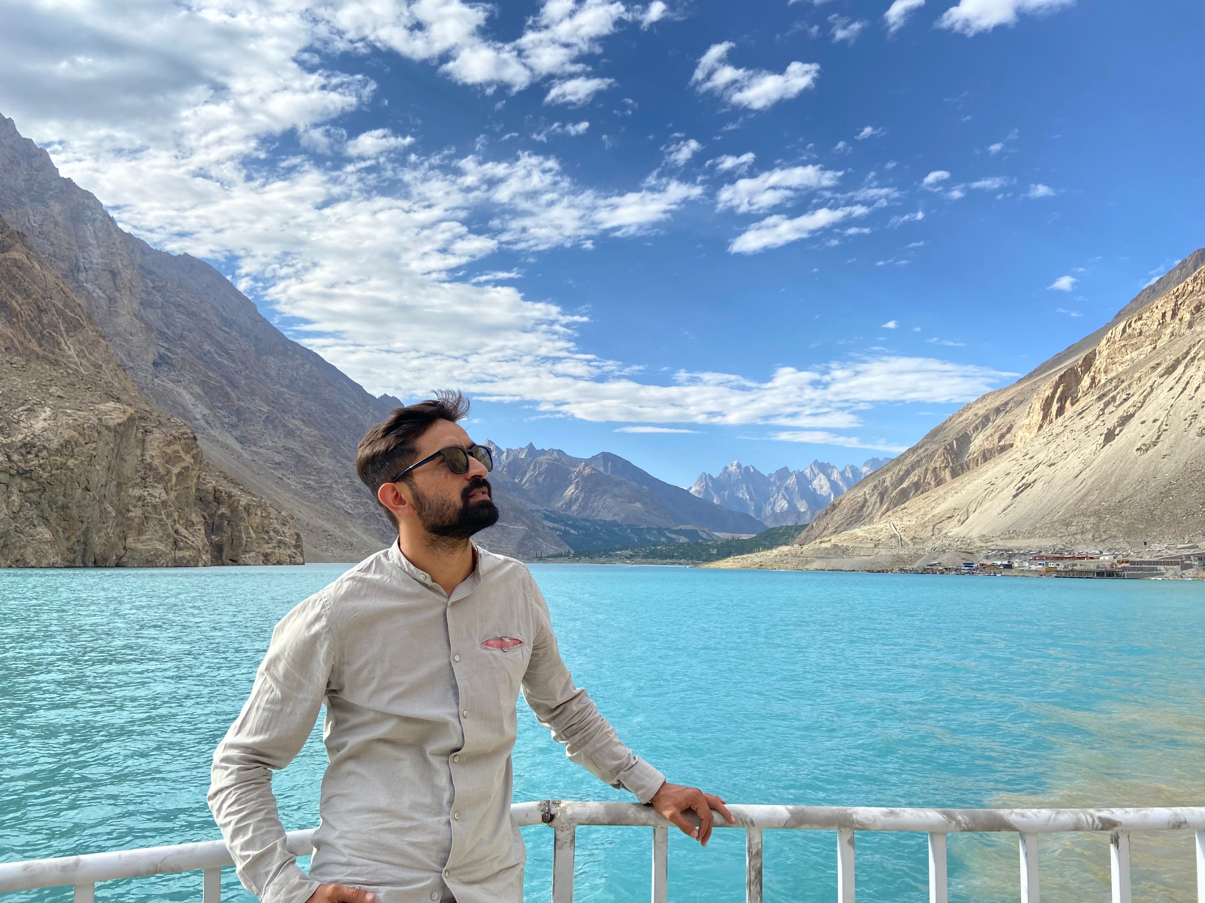 A man in sunglasses admires the turquoise waters and rugged mountains of Attabad, Pakistan.