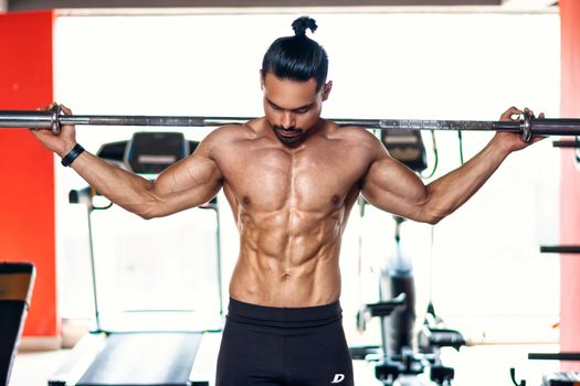 Strong and shirtless man lifting weights indoors in Pune gym.