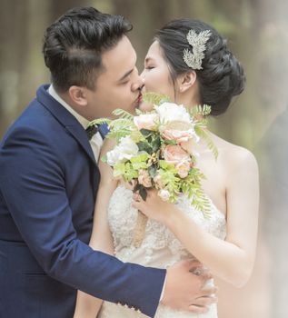 婚礼当天，一对优雅的情侣在户外手握花束接吻