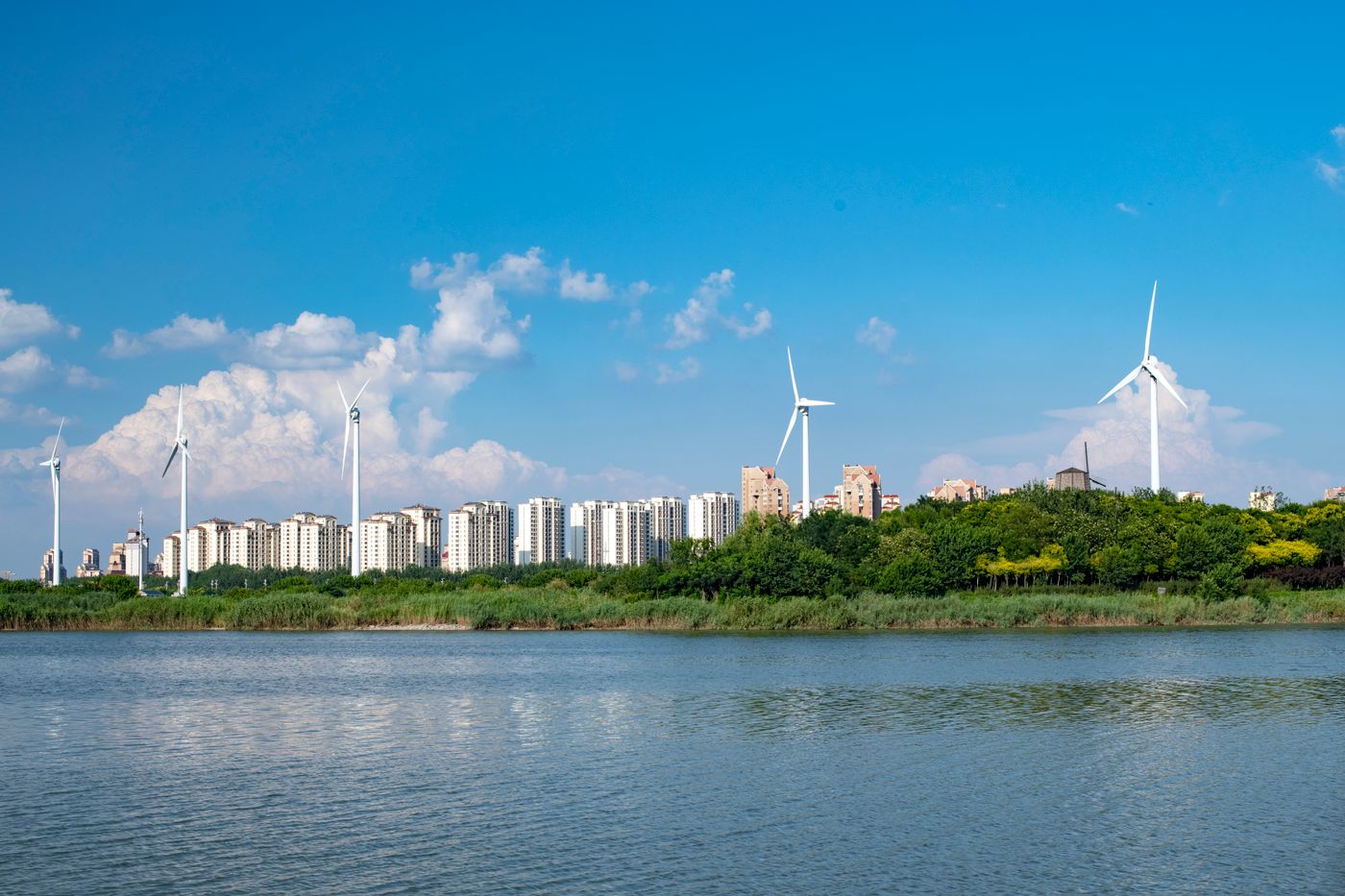 Wind turbines generate clean energy near an urban area with waterfront view.