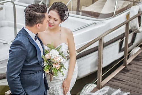 新婚夫妇站在船附近的棕色木码头上