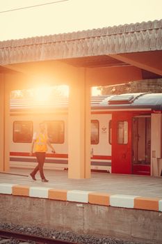 Sunset view of a train station platform with a worker in the foreground and a train in the background.