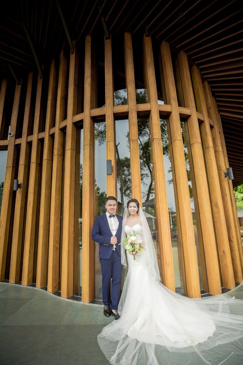 Photography of Couple Stands in Front Wooden Wall