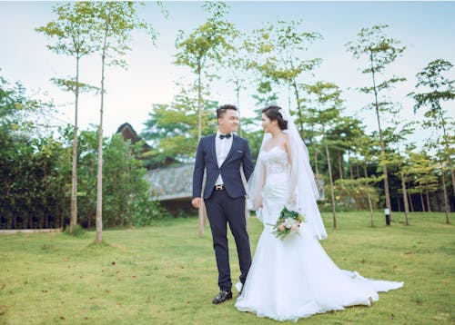 Bride and Groom Standing on Green Grass Surrounded by Green Leafed Trees