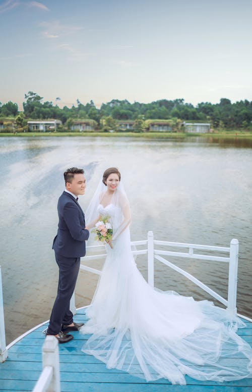 免费 刚结婚的男人和女人在水体附近的蓝色平台上 素材图片