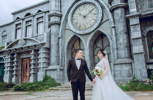 Free Groom Holding Bride's Hand Walking Near Cathedral Stock Photo