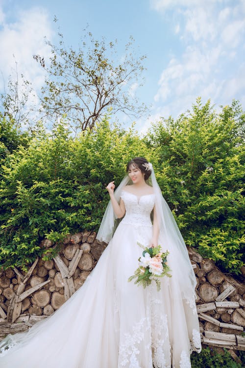 免费 新娘捧着花束站在前绿叶植物 素材图片