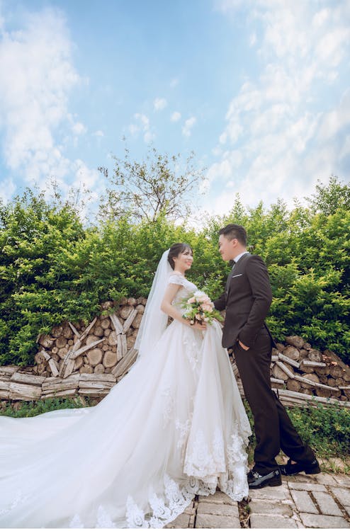 Bride and groom standing together in a lush garden, exchanging smiles on a sunny day.