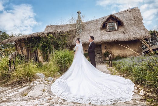 新娘和新郎身着优雅服装，在一处以农舍为背景的乡村户外场所摆好姿势