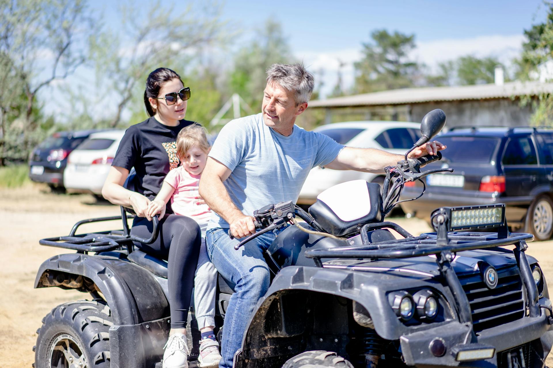 Family of three riding a quad bike outdoors in the sunny summer day.