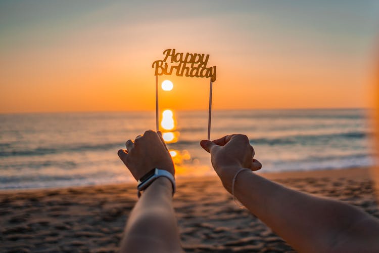 Hands Holding Happy Birthday Sign Towards Sunset Over Sea