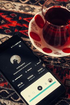 Overhead view of a vintage cup of tea next to a smartphone on a patterned surface, creating a cozy atmosphere.