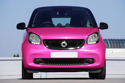 Front view of a bright pink smart car parked outdoors, highlighting its compact design.