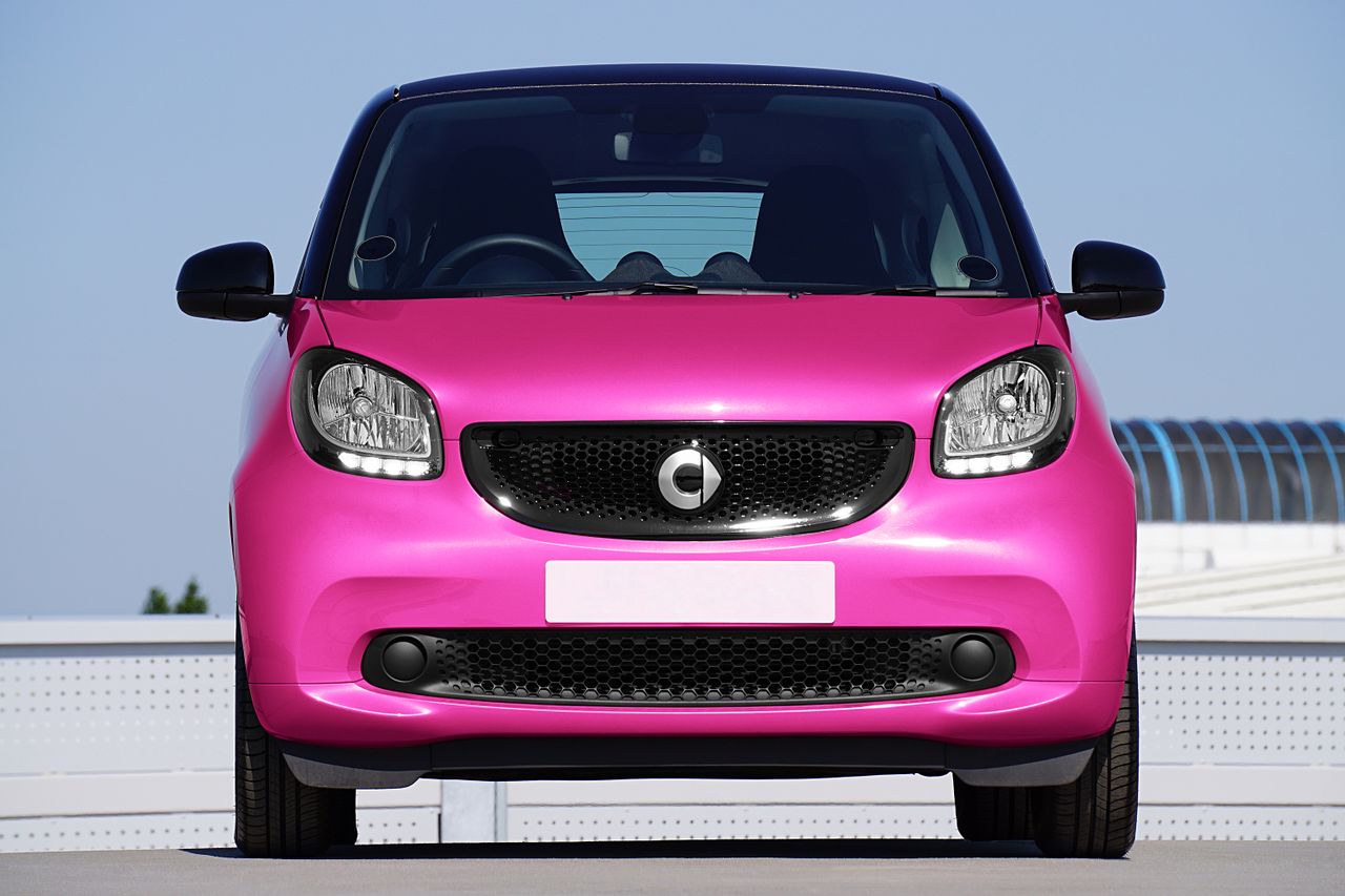 front view of a bright pink smart car parked outdoors highlighting its