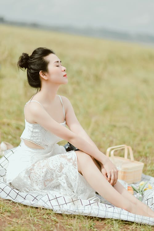 A Woman in White Dress Sitting on Grass Field