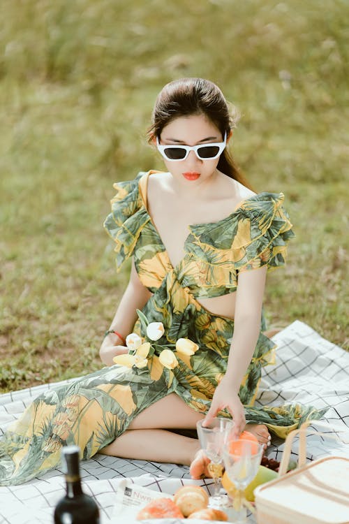 Young Beautiful Woman in a Summer Dress Sitting on a Picnic Blanket 