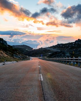 Empty road in Serra da Estrela, Portugal, at sunset with colorful clouds and mountain views.