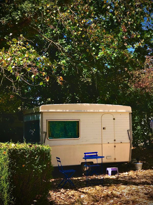 Vintage caravan parked among trees and bushes with camping chairs set out