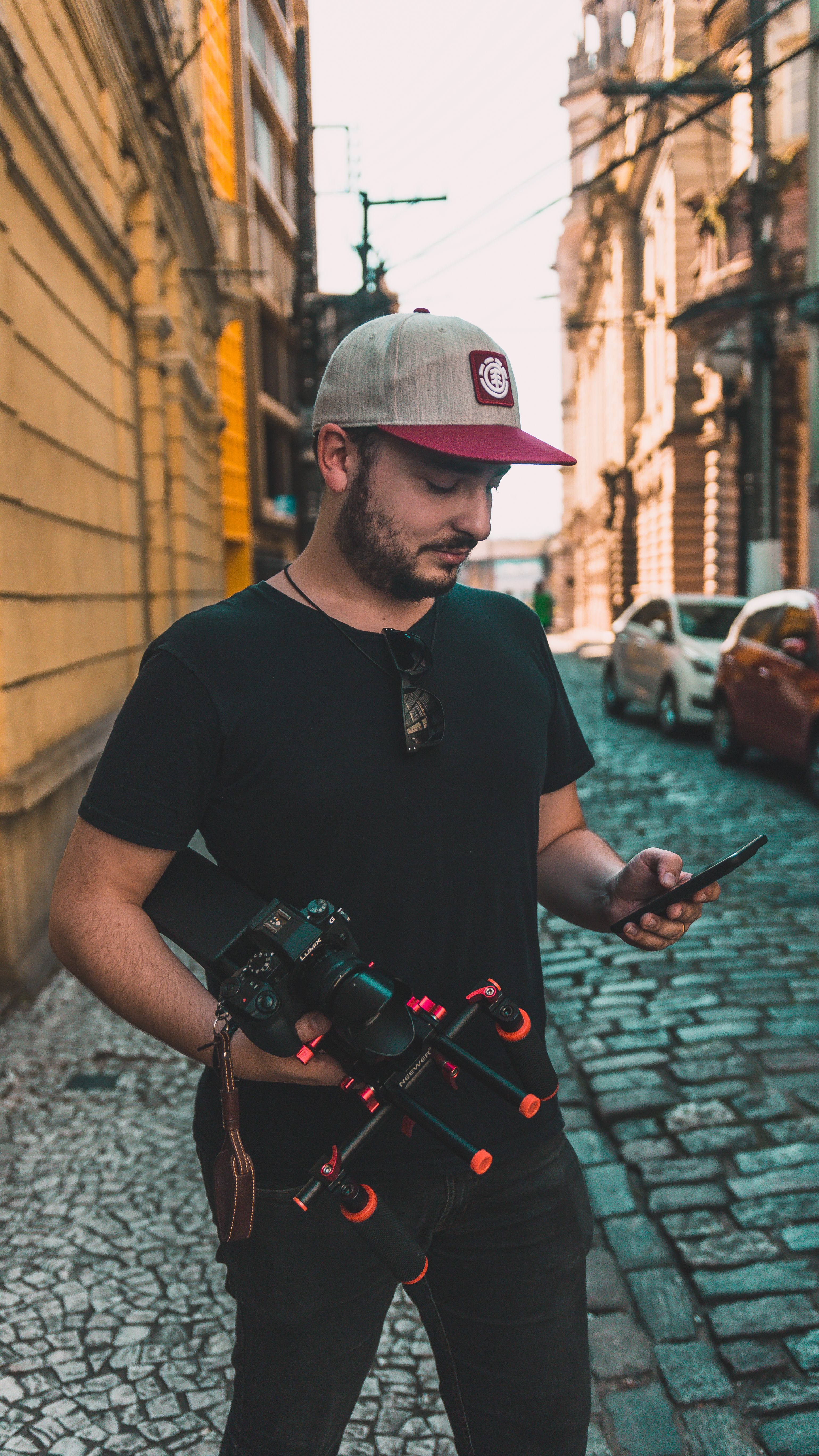 Filmmaker holding a camera and phone on a sunny street in Centro, SP, Brazil.