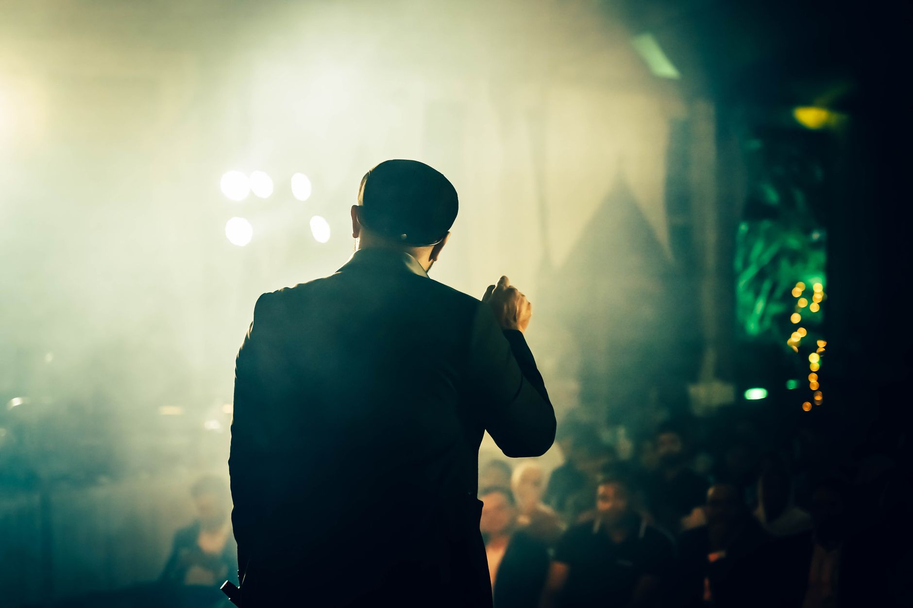 A man seen from the back speaking to an audience at an atmospheric entertainment venue.