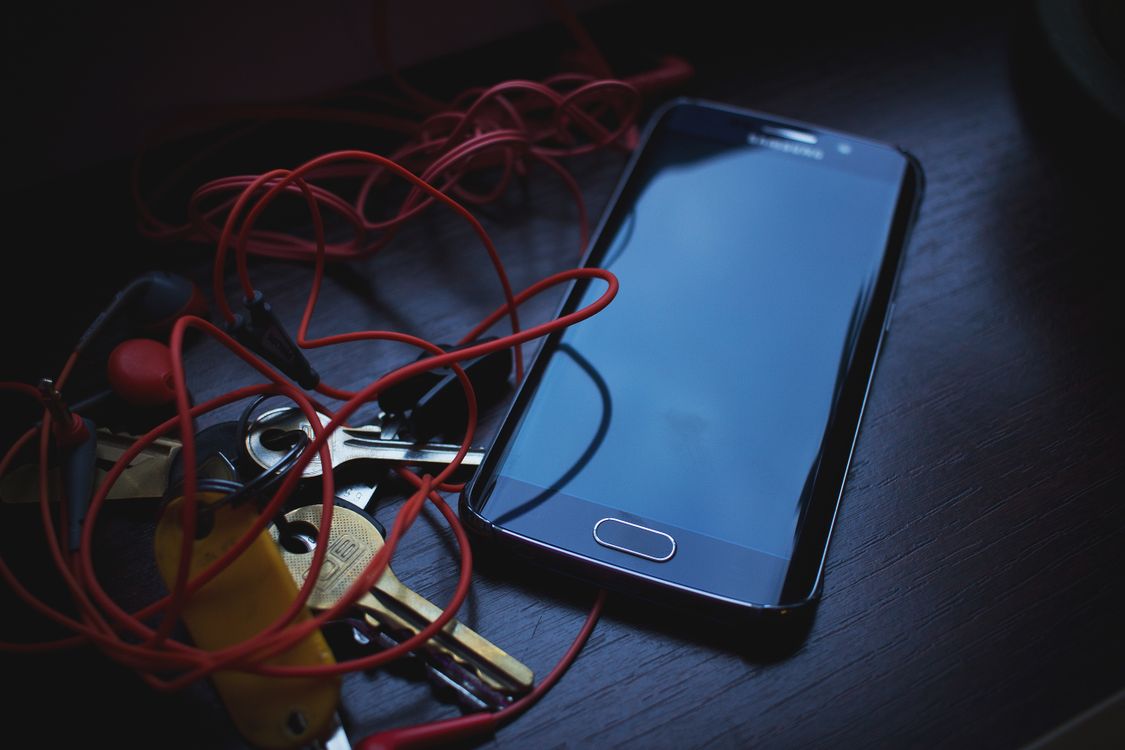 Nahaufnahme eines Smartphones, roter Kopfhörer und Schlüssel auf einem dunklen Holztisch.