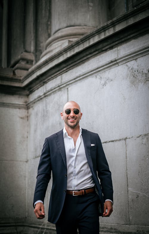 A Man in Black Suit Jacket Wearing Sunglasses Smiling at the Camera