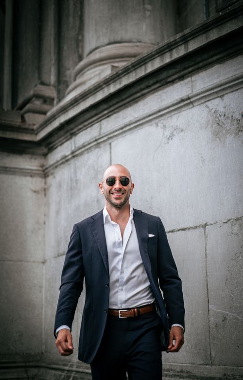 Free A confident man in a black suit smiling while walking outside, exuding sophistication. Stock Photo