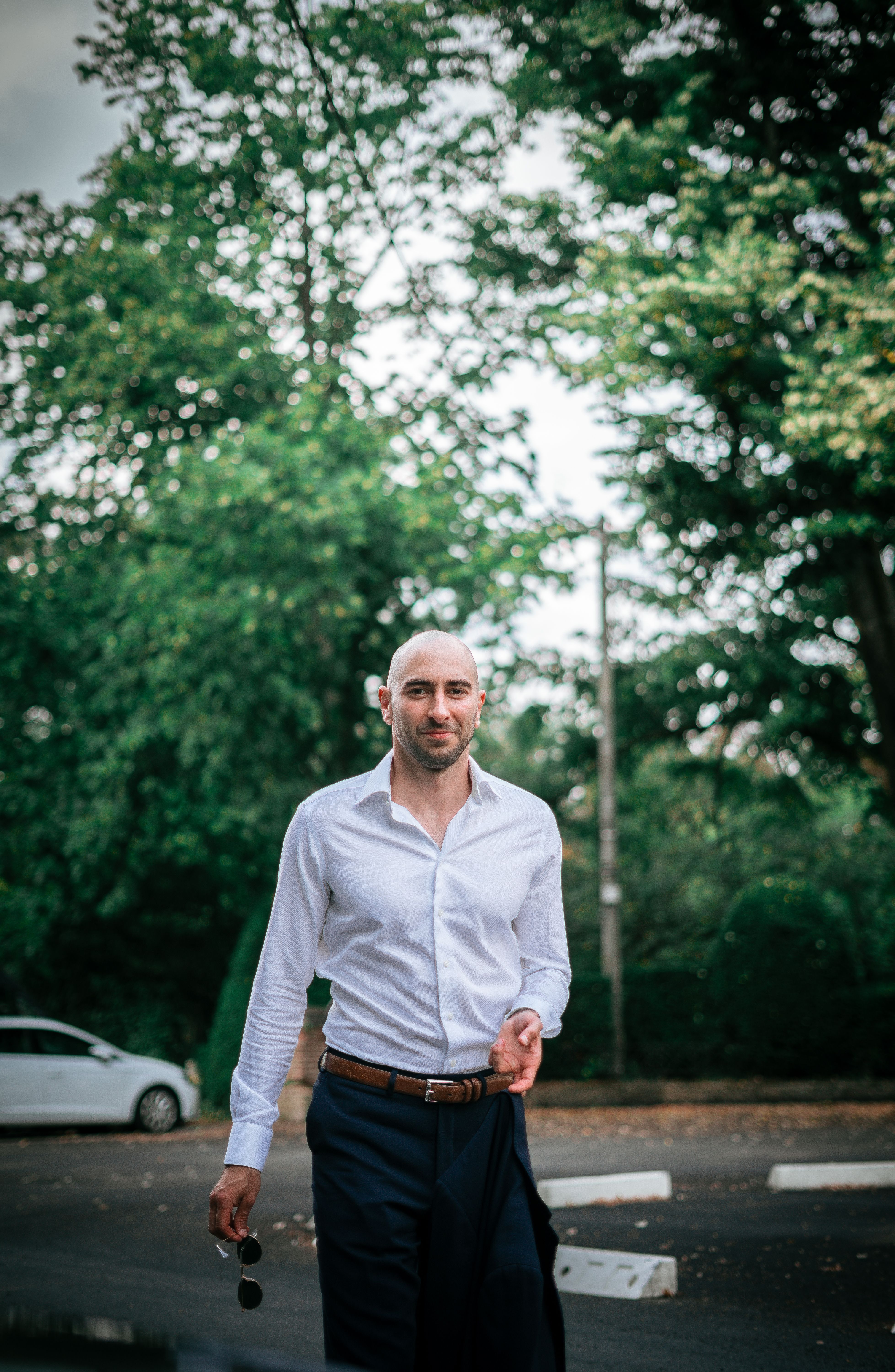 A bald man in an elegant outfit walking on a tree-lined street in Namur.