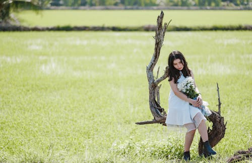 Woman Carrying White Flower Bouquet Sitting on Leafless Tree