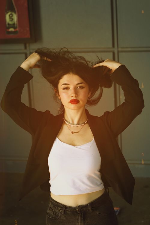 Free Young woman in black blazer and white crop top striking a confident pose indoors with bold red lips. Stock Photo
