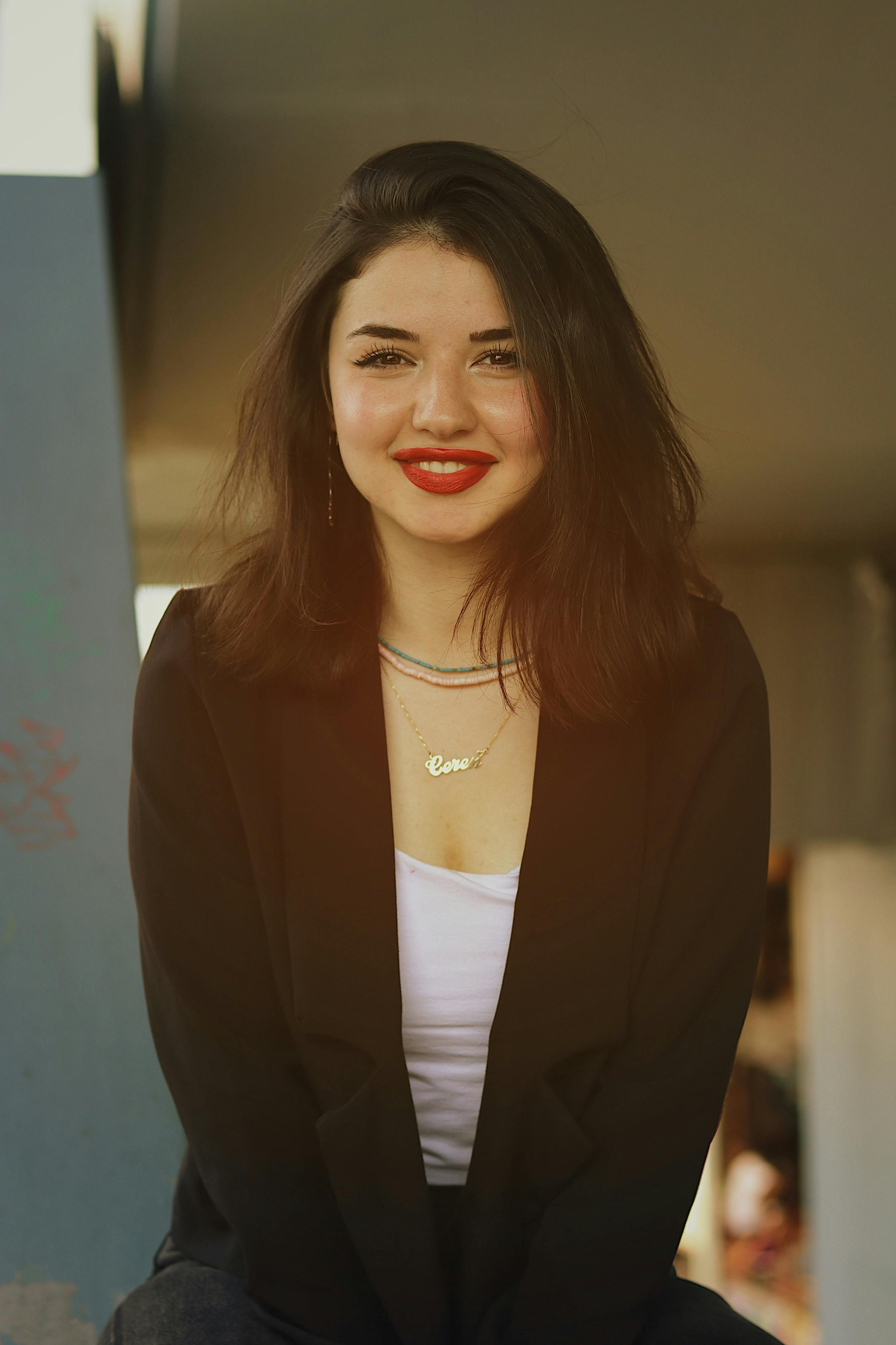 A fashionable young woman wearing a black blazer poses confidently with a bright smile.