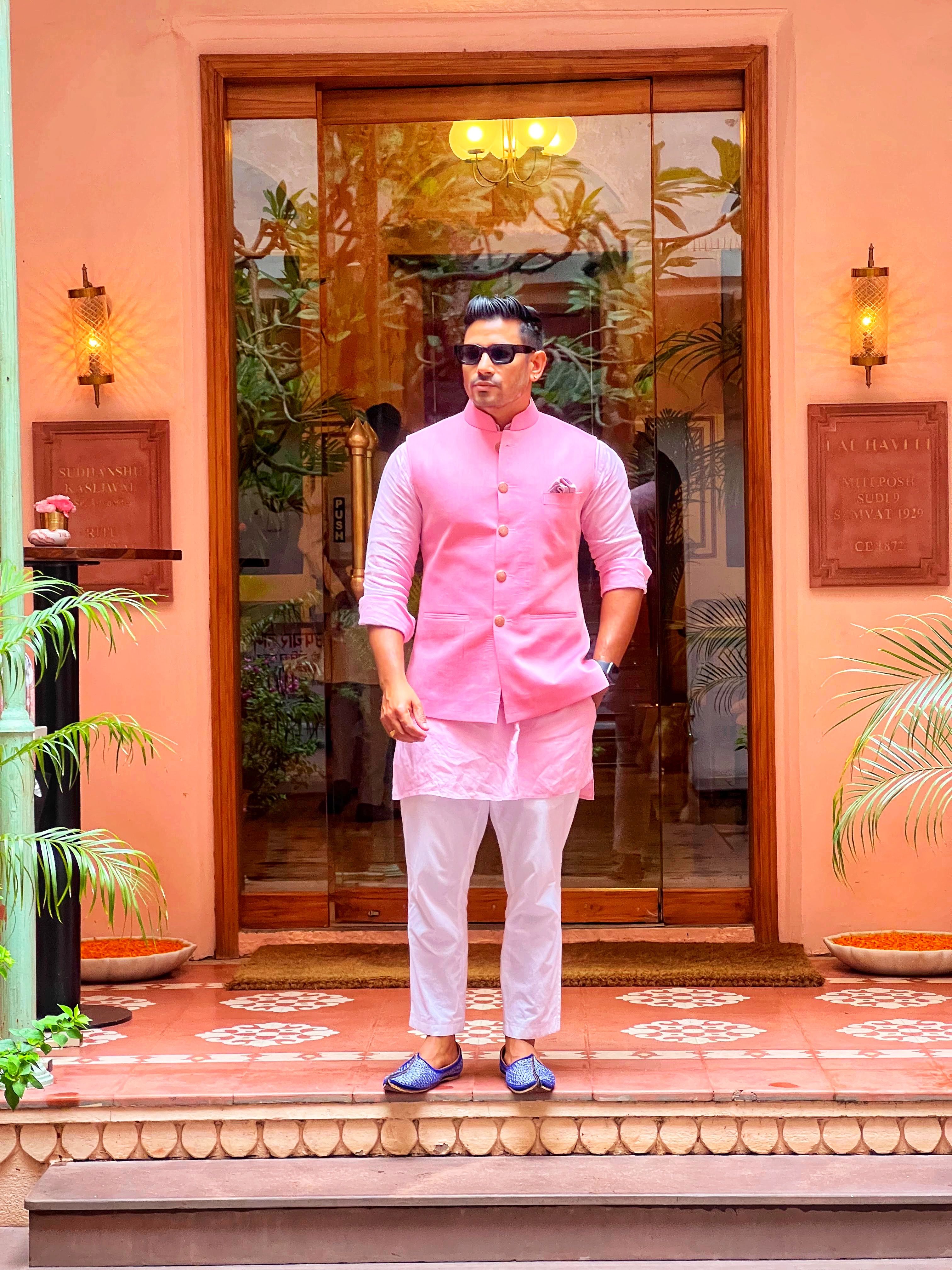 Fashionable man in pink kurta and sunglasses standing at a decorative entryway in Jaipur, India.