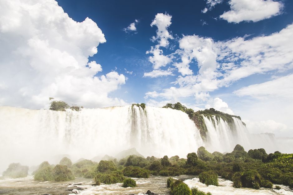 Stunning view of Iguazu Falls cascading amidst lush greenery under a bright summer sky.